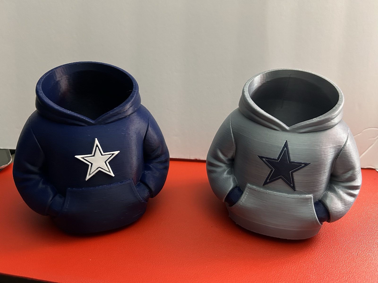 Two printed hoodie can coolers, navy and silver, with a star on the chest