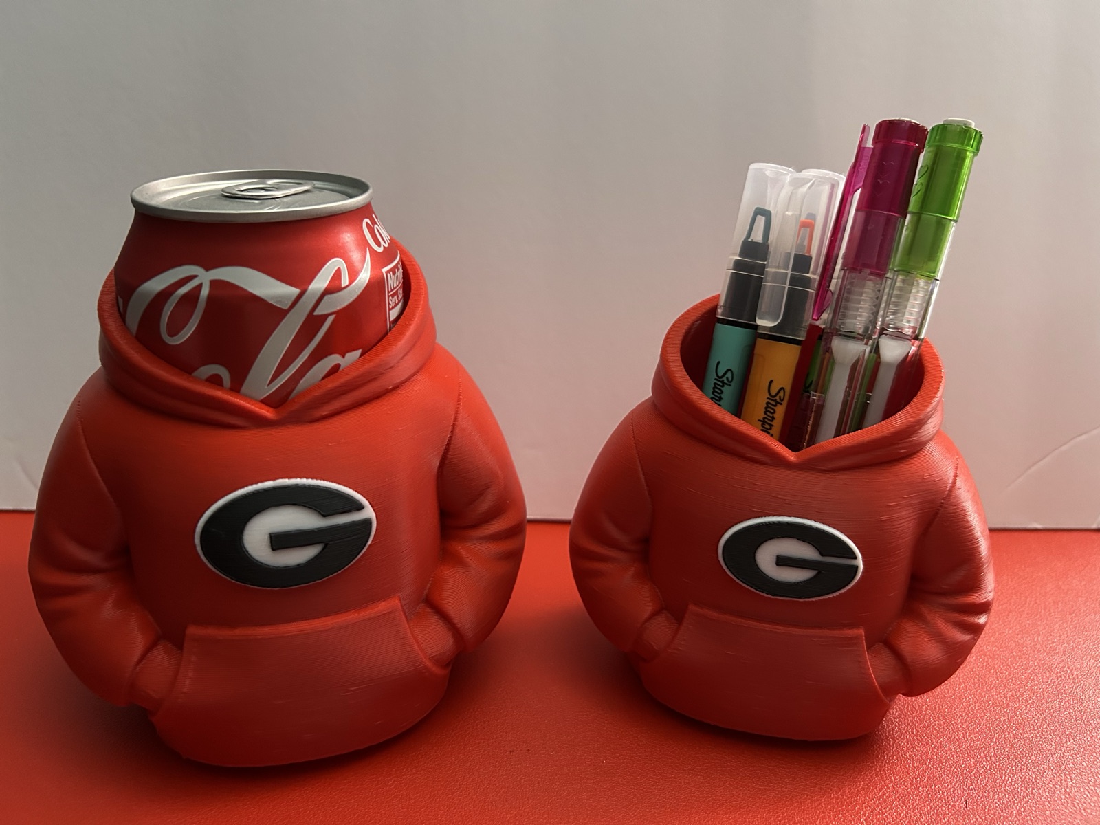 Hoodie can cooler holding a 12 oz can beside a hoodie pen holder